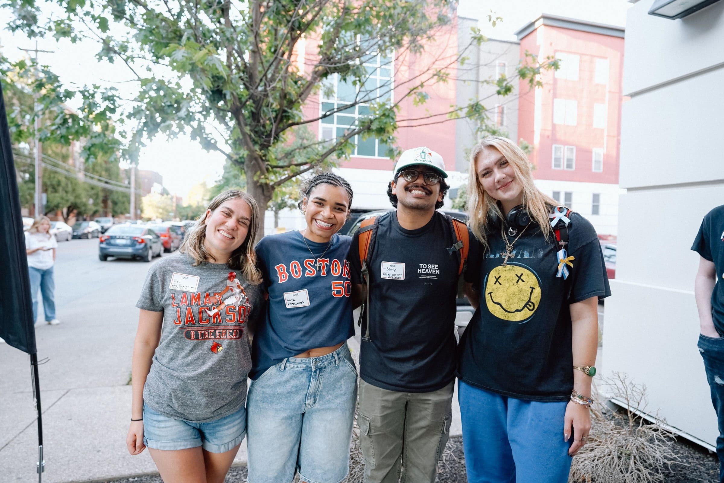 Four students standing together on a campus street, wearing name tags