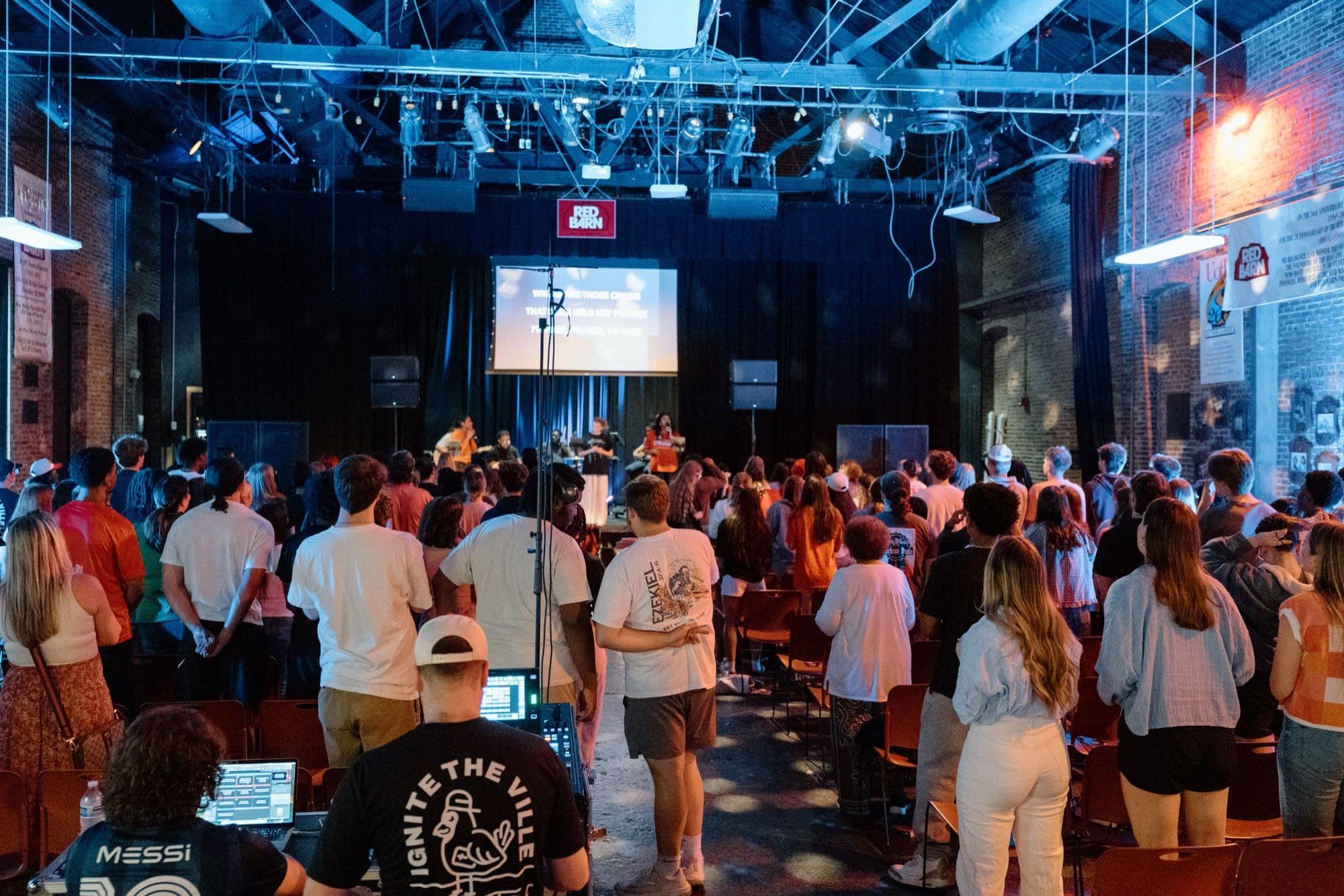 A room full of students standing and singing together at a worship night