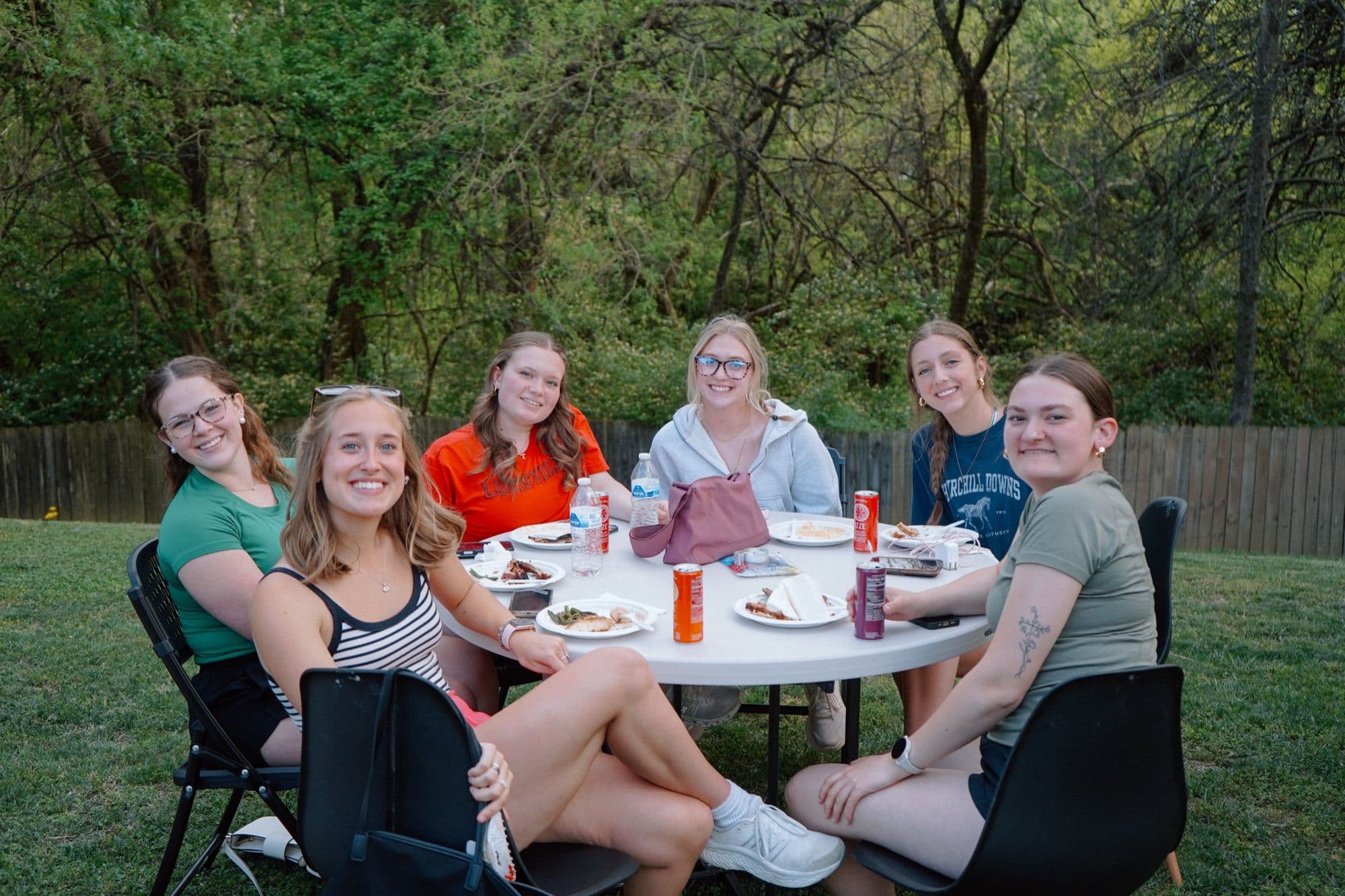 Six students sitting around a table outdoors, sharing a meal